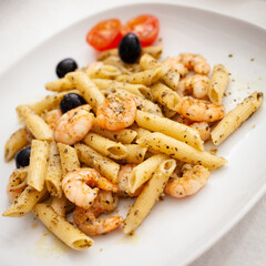 Penne Pasta with Prawns or Shrimps, olives, tomatoes and spices on white plate. Healthy sea food for the family.