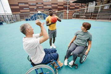 Mature couple in wheelchairs learning to play basketball together with the coach