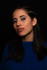 Naklejka premium Latin woman. model, young with light skin, tanned. model. with continuous light, shadows and ring of light. Model with eye makeup. green eyes. on black background. dressed in blue. portrait, model.