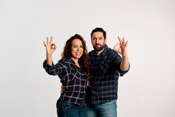 An adult couple in plaid shirts showing thumbs up to the camera and smiling against a white background - 463493034