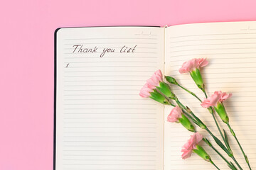 Above view of flowers on open paper notepad with handwritten words Thank you list. Gratitude journal concept