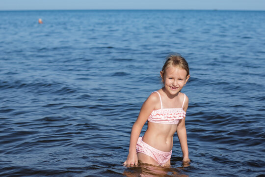 girl at the sea, 7 years old, blonde, in a bikini stands in the water, children's portrait, summer seascape