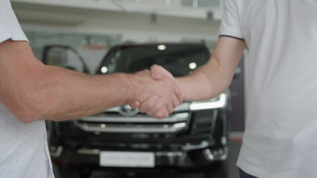 car service, satisfied male customer shakes hands tightly confirming car deal in car showroom