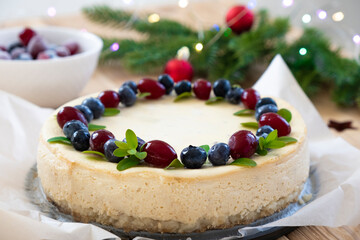 Festive cake for Christmas holidays. Homemade cheesecake decorated with blueberry and cranberry with fir branches in Christmas lights bokeh on background. Dessert for New Year and Christmas menu.