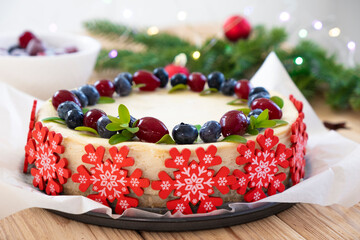 Festive cheesecake for New Year and Christmas holidays. Homemade cake with berries decorated by sugar snowflakes with fir branches in Christmas lights bokeh on background. Vegan gluten free dessert.