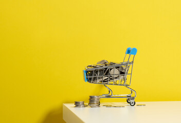miniature metal shopping cart and a stack of coins on a white table. The concept of discounts and...