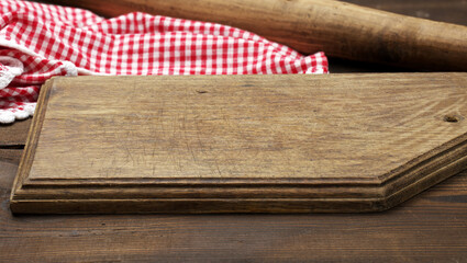 empty old wooden cutting board and folded red and white cotton kitchen napkin on a wooden brown...