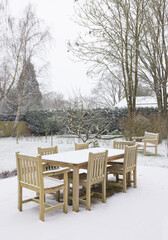 Fototapeta na wymiar Snow falling on garden patio furniture in winter, UK