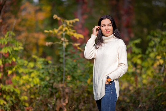 A young girl stands straightening her hair in an autumn park in a white sweater and blue jeans. High quality photo