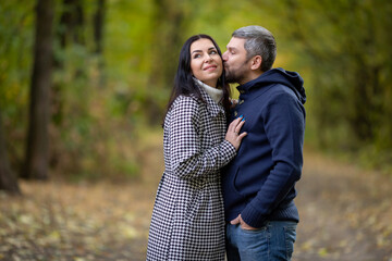 A guy hugs and kisses a girl standing in an autumn park. High quality photo
