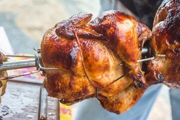 roasted chicken with chicken machine in the background, copy space and natural light, man holding a skewer with several chickens