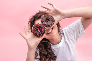 Pretty smiling woman holding donuts in her hands on a pink background.