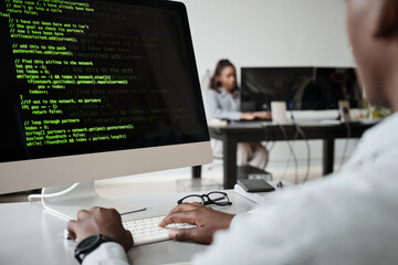 Close up of African-American software developer writing code while using computer in office, copy...