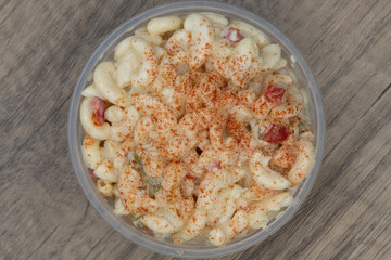 Overhead view of generous portion side order of macaroni salad in a clear plastic bowl to compliment your meal