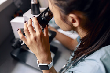Scientist looks into microscope researching material sample at table in laboratory