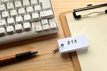 There is a word book with the word of BTA which is an abbreviation for Behavioral Targeting Advertising on the desk with a pen and a keyboard.