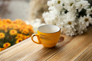 Yellow cup on a wooden surface on a blurred background with flowers.