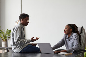 Minimal side view portrait of two African-American young people chatting in office while discussing...