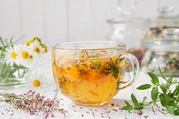 Glass cup of healthy calendula herbal tea, healing heather, chamomile and salvia medicinal herbs...