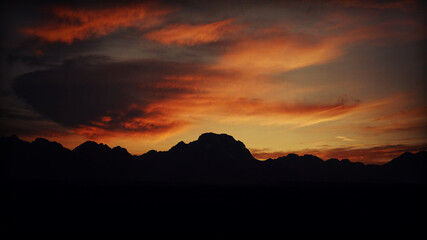 Deep red and orange sunset over the silhouette of the grand tetons in grand teton national park in...