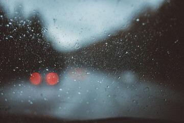 macro of rain droplets on a windowshield with bokeh of trees, highway, and car taillights out of focus