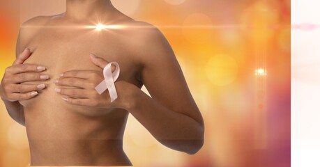 Mid section of woman wearing a pink ribbon on her chest against spots of lights on orange background - Powered by Adobe