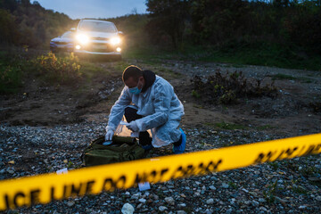Forensic police investigator collecting evidence at the crime scene in nature at night