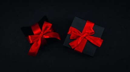 Two black small gift boxes with a red ribbon tied in a bow