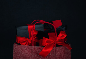 One red shiny bag with three gift boxes on a black background.