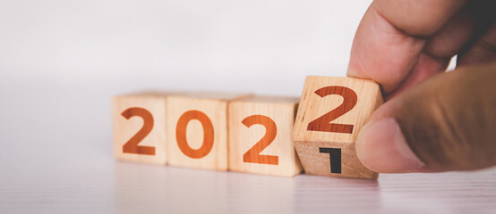 Hands flipping cube wooden block with text year 2022, beginning and trend, calendar and time,...
