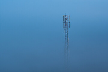 Mobile phone tower sticking out of dense fog.