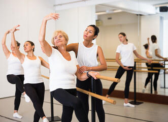 Fototapeta na wymiar Various aged women exercising ballet dance moves. Woman trainer correcting her students.