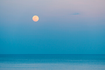Full moon over the sea against the background of the colorful sky