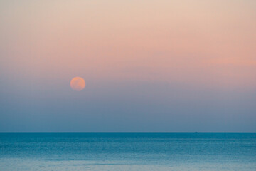 Full moon over the sea against the background of the colorful sky