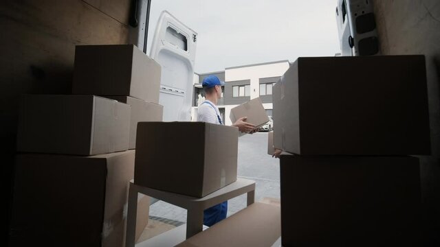 Two young workers of removal company unload boxes and furniture from minibus into customer's home