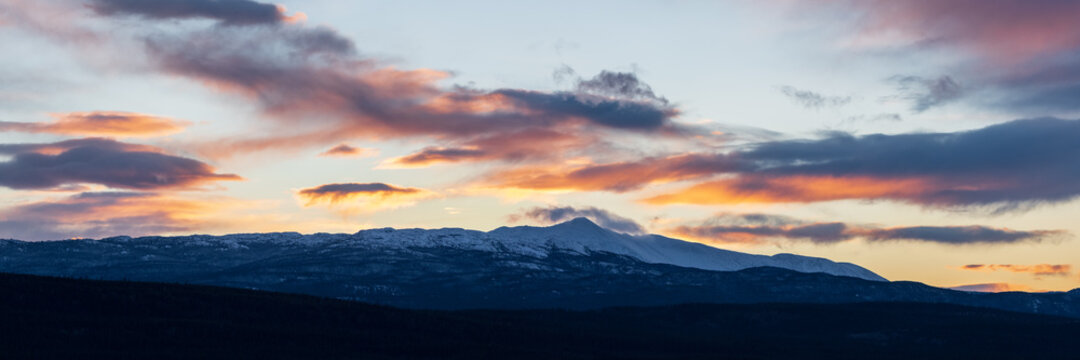 Sunset over boreal forest in northern Canada with dark theme. Snow capped mountains, pink, pastel sky. 