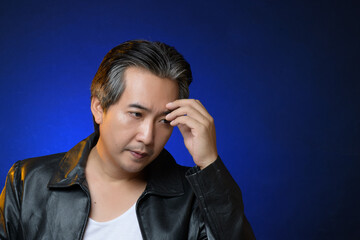 Portrait of thoughtful smart middle  asian man thinking in dark and blue light background. Senior man felling serious