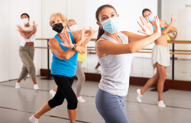 Fototapeta na wymiar Women in protective mask practicing vigorous dance movements in group dance class