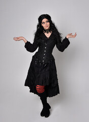 Full length portrait of dark haired woman wearing  black victorian witch costume with corset, ...