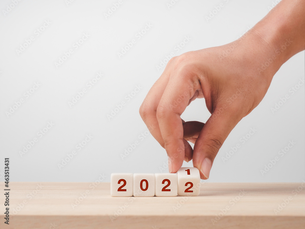 Poster hand turning a dice with calendar year numbers from 2021 to 2022 on a wood table and white backgroun
