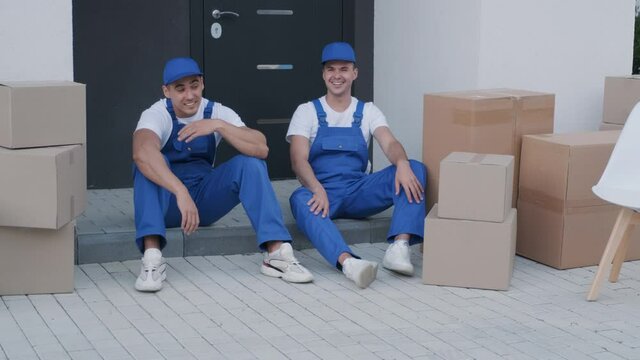 Two removal company workers have a break while sitting on the step