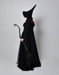 Full length portrait of dark haired woman wearing  black victorian witch costume with  cloak and...