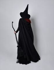 Full length portrait of dark haired woman wearing  black victorian witch costume with  cloak and...