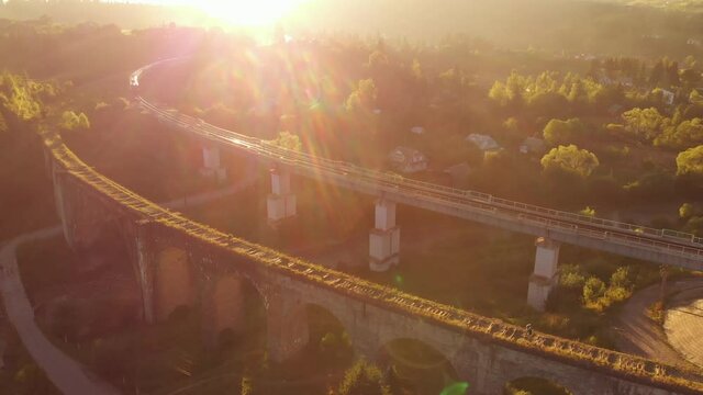 Aerial shot of a train crossing a beautiful stone bridge at sunset