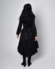 Full length portrait of dark haired woman wearing  black victorian witch costume.  standing pose,...