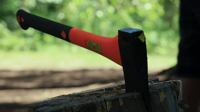Man slams axe into stump after chopping wood, walks away. Close up, waist level.