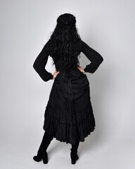Full length portrait of dark haired woman wearing  black victorian witch costume.  standing pose,...
