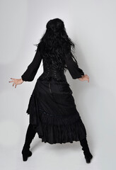 Full length portrait of dark haired woman wearing  black victorian witch costume.  standing pose,...