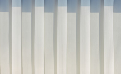 Fototapeta premium Abstract geometric vertical lines white and gray gradient color. Repeating pattern, background texture, design of striped lines. Blinds illuminated by the sun, close-up.