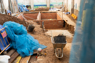 View of building under reconstruction - tools and materials near pit with brick construction